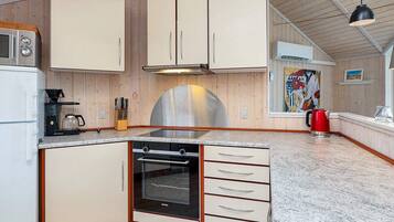 A kitchen with wooden cabinets, a stainless steel range hood, a coffee maker, and a red kettle.