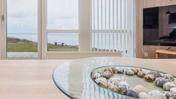 A modern interior with a large window overlooking a body of water, a wooden floor, and a glass table with decorative stones.