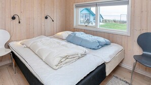 Ett rum med en säng, en stol, ett fönster och utsikt över ett hus.