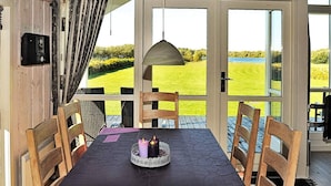 A dining area with a table set for two, chairs, a candle centerpiece, and a view of a green landscape through large windows.