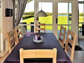 A dining area with a table set for two, chairs, a candle centerpiece, and a view of a green landscape through large windows. - 4 Star Holiday Home in Ansager (Ansager)
