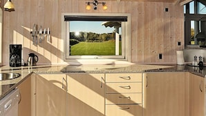 A modern kitchen with wooden cabinets, a large window, and a view of a green field.