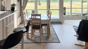 A dining area with a table and chairs, a view of a field through large windows, and a wooden floor.