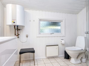 A small, white-paneled bathroom with a toilet, a window, a radiator, and a water heater.