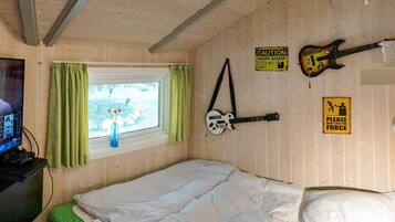 Un dormitorio con cama, ventana con cortinas, una guitarra y un televisor sobre un escritorio.