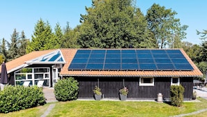 Ein Haus mit einer Solaranlage auf dem Dach, einer überdachten Terrasse und einem kleinen Garten.