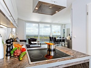A modern kitchen with a built-in stove, a dining area with a view, and a large window. - Holiday Home in Wendtorf (Schönberg)