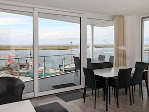 A modern room with a large sliding glass door leading to a balcony with a view of the water and boats. - Holiday Home in Wendtorf (Schönberg)