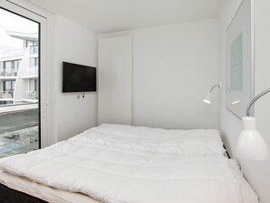A modern bedroom with a large bed, a mounted TV, a bedside lamp, and a view of the outside. - Holiday Home in Wendtorf (Schönberg)