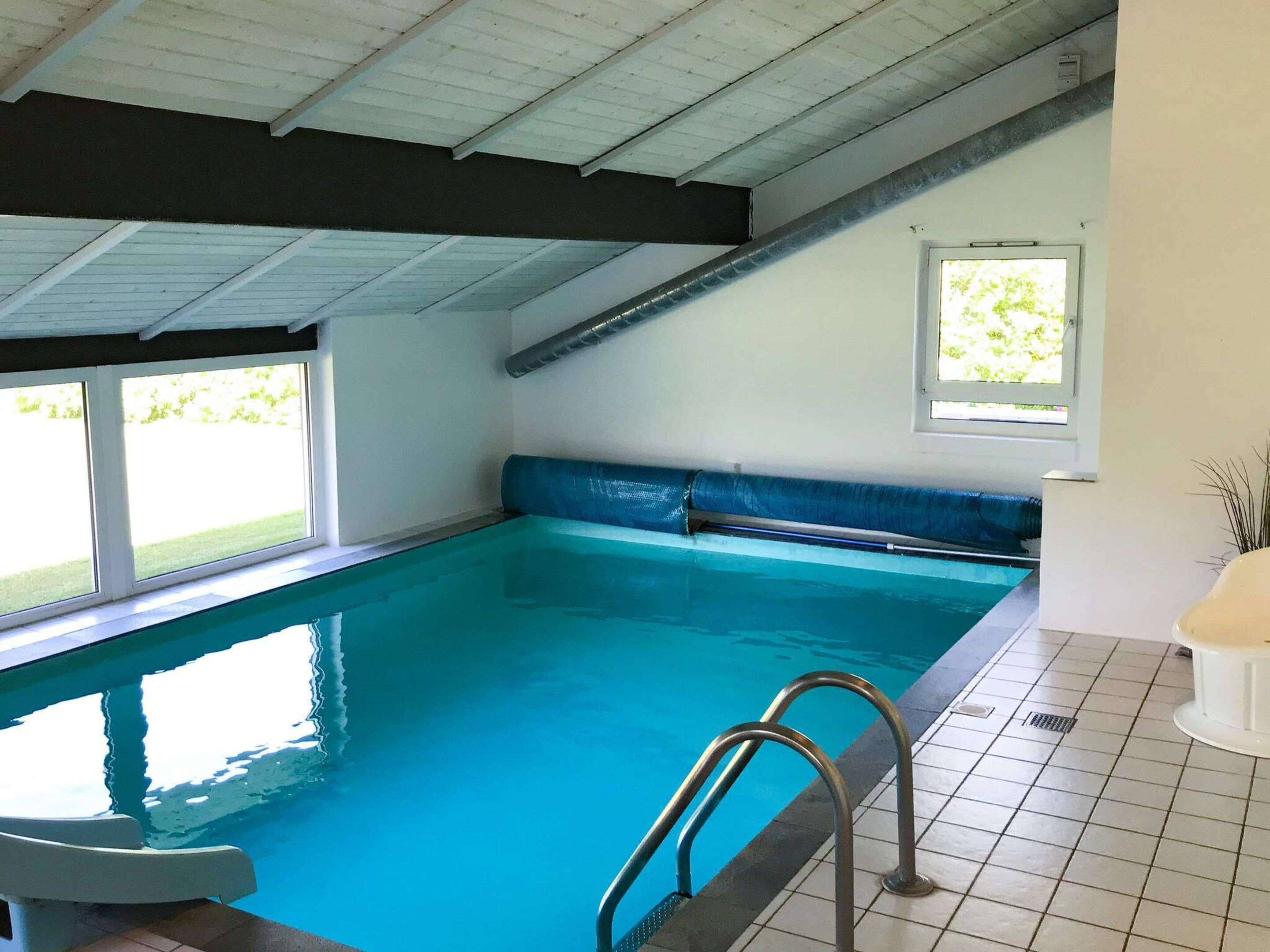 An indoor swimming pool with clear water, a metal ladder, and a window with a view of greenery.