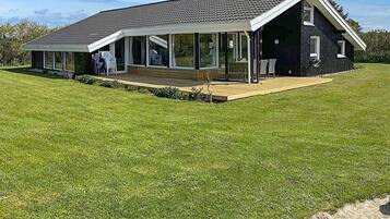 A modern house with a large deck, a covered patio, and a well-maintained lawn.