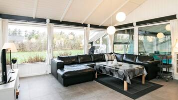 A modern living room with a sectional sofa, a coffee table, and large windows offering a view of the outdoors.