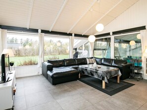 Un salon moderne avec un canapé d’angle, une table basse et de grandes fenêtres donnant sur l’extérieur.