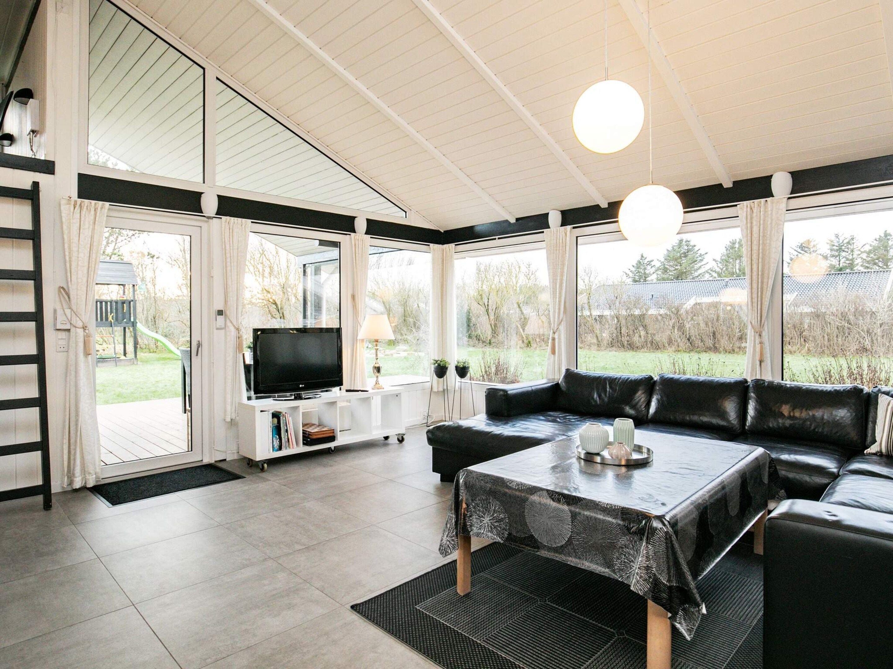 A modern living room with a black leather sofa, a television on a white stand, and a dining table with a black tablecloth.