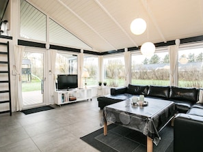 Un salon moderne avec un canapé en cuir noir, un téléviseur posé sur un meuble blanc et une table à manger recouverte d’une nappe noire.