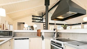 A modern kitchen with a dishwasher, stove, and microwave. There is a large window above the sink and a potted plant on the counter. - 4 Star Holiday Home in Hjorring (Hjørring)