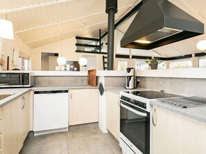 A modern kitchen with a dishwasher, stove, and microwave. There is a large window above the sink and a potted plant on the counter. - 4 Star Holiday Home in Hjorring (Hjørring)