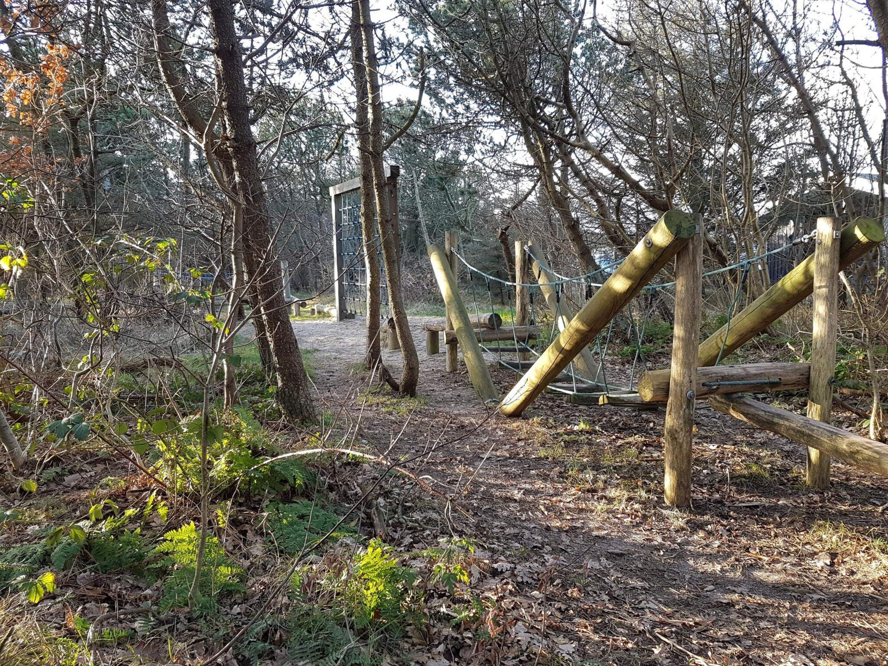 Un área boscosa con una estructura de madera para escalar y una cerca de metal.