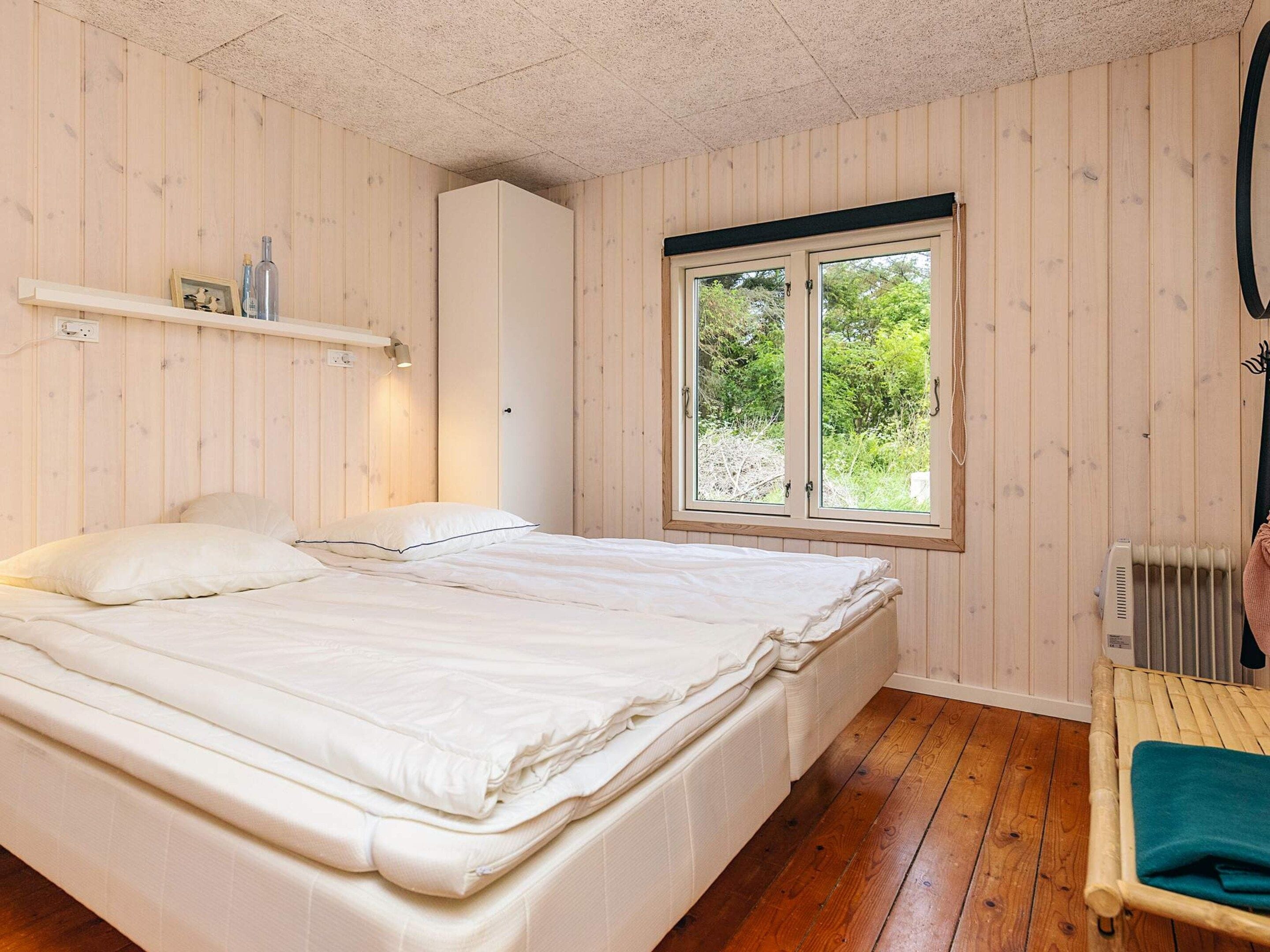 A bedroom with a bed, a window, a radiator, and a shelf with items.