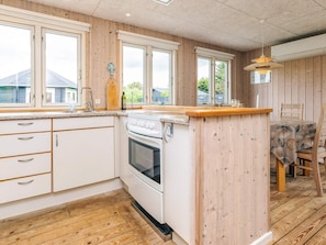 A kitchen with wooden paneling, a white stove, and a dining area with a table and chairs. - Lovely Holiday Home in LÃ¸nstrup near Sea (Hjørring)