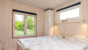 A bedroom with a bed, wooden walls, a window, and a wall-mounted light fixture.