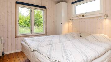 A bedroom with a bed, wooden walls, a window, and a wall-mounted light fixture.