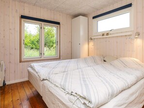 A bedroom with a bed, wooden walls, a window, and a wall-mounted light fixture.