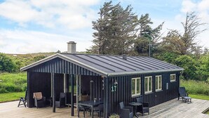 A small, dark-colored cabin with a covered patio area, featuring a table and chairs, and a number '17' on the side. - Lovely Holiday Home in LÃ¸nstrup near Sea (Hjørring)
