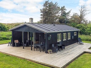 A small, dark-colored cabin with a covered patio area, featuring a table and chairs, and a number '17' on the side. - Lovely Holiday Home in LÃ¸nstrup near Sea (Hjørring)