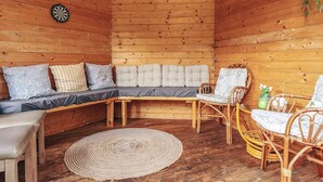 Interior acogedor de una cabaña de madera con un sofá modular, sillas de mimbre, una alfombra tejida y un dardo.