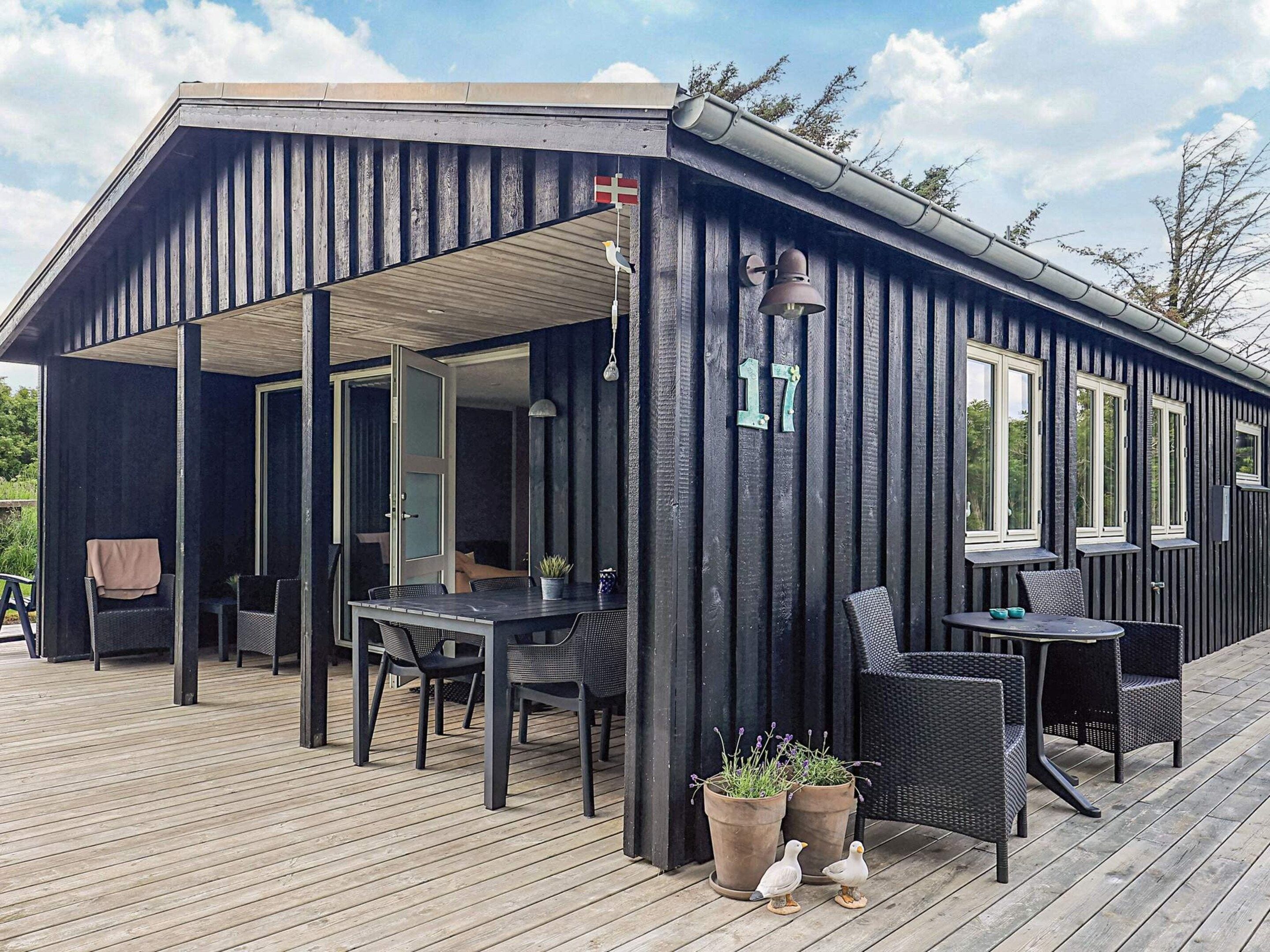 A covered outdoor seating area with tables and chairs, a wooden deck, and a building with a dark exterior and a visible number '17'.