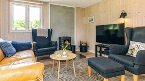 A cozy living room with a leather sofa, a black armchair, a wooden floor, a fireplace, and a television.