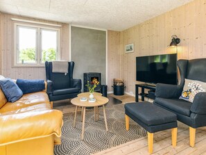 A cozy living room with a leather sofa, a black armchair, a wooden floor, a fireplace, and a television.