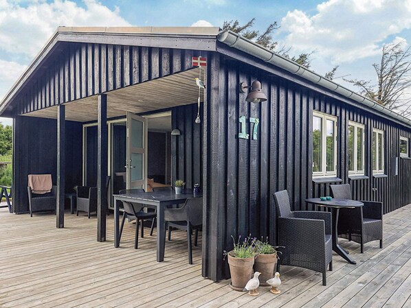 A covered outdoor seating area with tables and chairs, a wooden deck, and a building with a dark exterior.