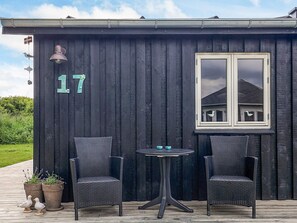 A dark wooden building with the number 17 on the wall, two wicker chairs, a small round table, and two potted plants.