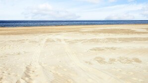 A wide sandy beach with footprints and tire tracks, leading to the ocean under a partly cloudy sky. - 5 Star Holiday Home in Lokken (Lokken)