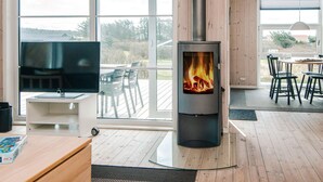A modern living room with a large window, a fireplace, a TV, and a dining area. - 5 Star Holiday Home in Lokken (Lokken)