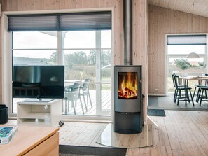Ein modernes Wohnzimmer mit großem Fenster, Kamin, Fernseher und Essbereich.
