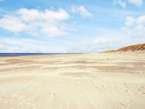 Ein weiter Sandstrand mit Fußabdrücken und Dünen im Hintergrund.