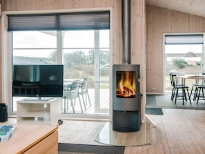 A modern living room with a large window, a fireplace, a TV, and a dining area. - 5 Star Holiday Home in Lokken (Lokken)