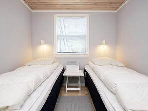 A small, single-room accommodation with two beds, a window with blinds, and a desk.