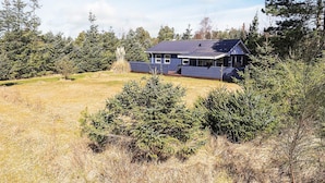 Yhden kerroksen talo, jonka ulkoseinät ovat tumman siniset, ja jota ympäröi ruohikkoalue ja tiheä metsä.