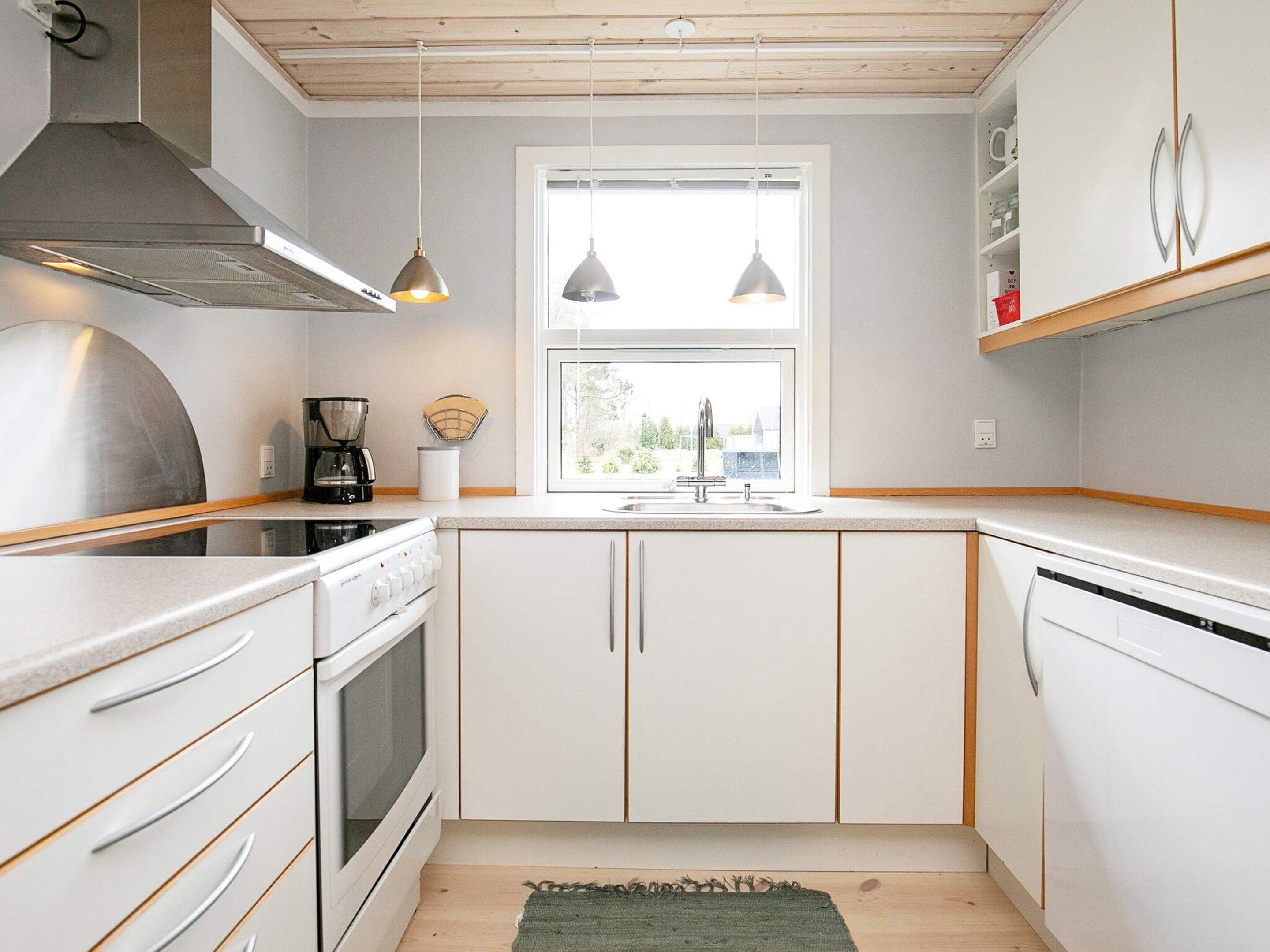 Cocina compacta con armarios blancos, horno integrado, cafetera e iluminación colgante.