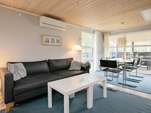 A modern living room with a dark grey sofa, a white coffee table, and a dining area with metal chairs and a glass table.
