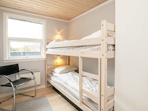 A bunk bed with a desk and chair, a window, and a wall-mounted lamp.