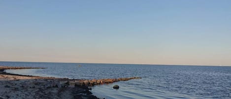 A beach with calm water, a rocky shoreline, and a clear sky.