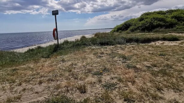 A beach with a lifebuoy attached to a post, a sign, and a clear sky.