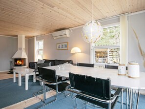 A modern living room with a fireplace, a dining table with chairs, a sofa, and a large window with a view of the outdoors. - 4 Star Holiday Home in Vaeggerlose (Vaeggerlose)