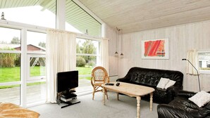 A living room with a black leather sofa, a wooden coffee table, a wicker chair, and a TV on a stand. - 6 Person Holiday Home in Hejls-by Traum (Hejls)