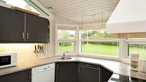 A modern kitchen with dark cabinets, a white microwave, a dishwasher, and a large window offering a view of a green garden. - 6 Person Holiday Home in Hejls-by Traum (Hejls)